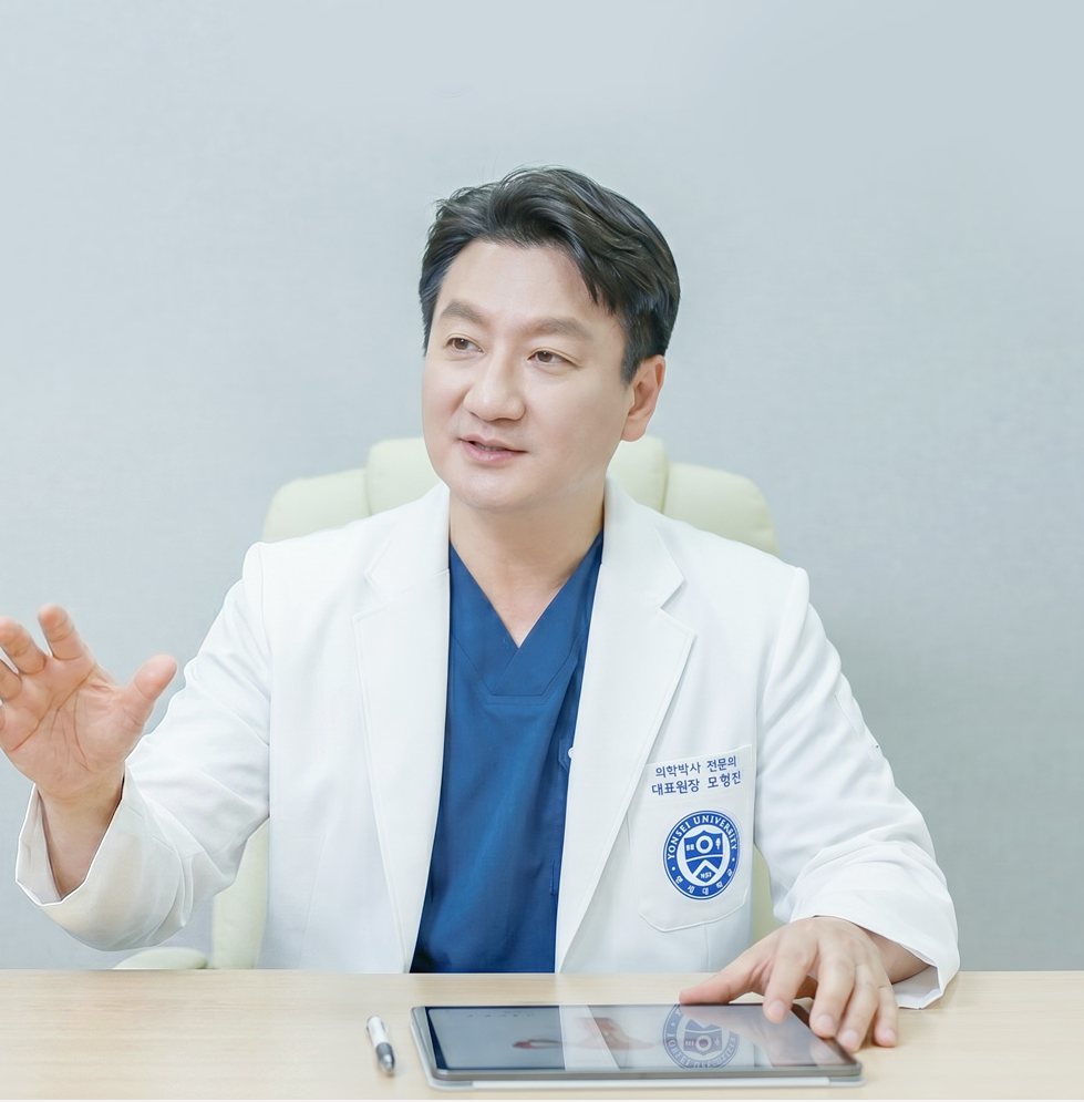 진료실 책상에서 손짓하며 설명하는 모형진 대표원장(태블릿)