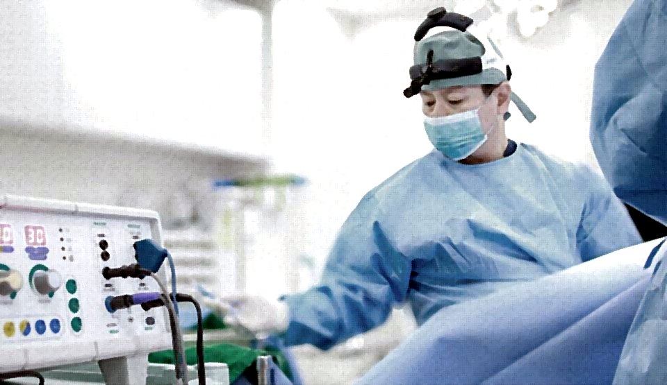 수술실에서 헤드라이트를 쓰고 수술하는 의료진(장비 옆)